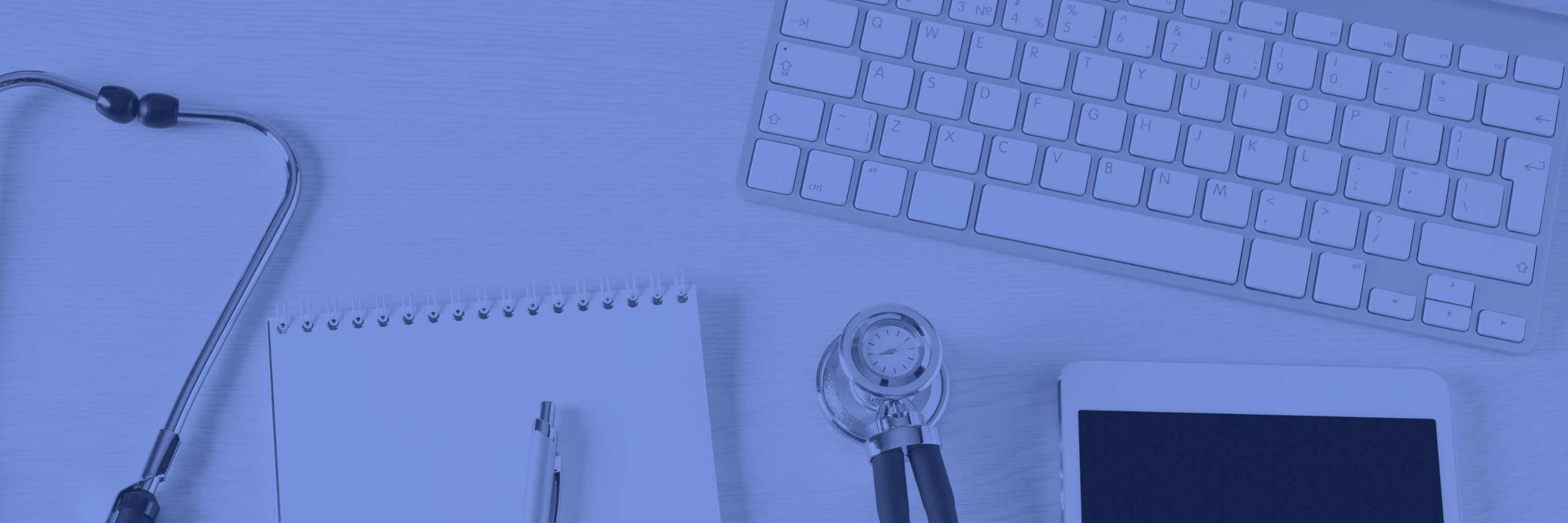 Stethoscope, pad, pen, tablet, and keyboard on a desk