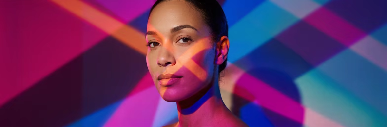 A woman's face lit by overlapping bands of pink, orange and blue light